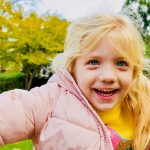 smiling girl with a pink coat on and a yellow jumper