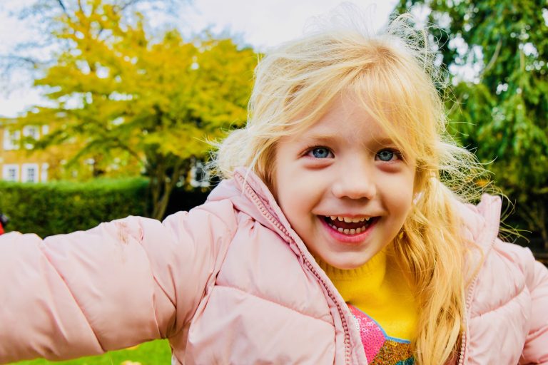 smiling girl with a pink coat on and a yellow jumper