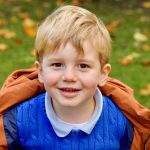 smiling child wearing a blue jumper and an orange coat