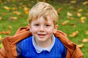 smiling child wearing a blue jumper and an orange coat