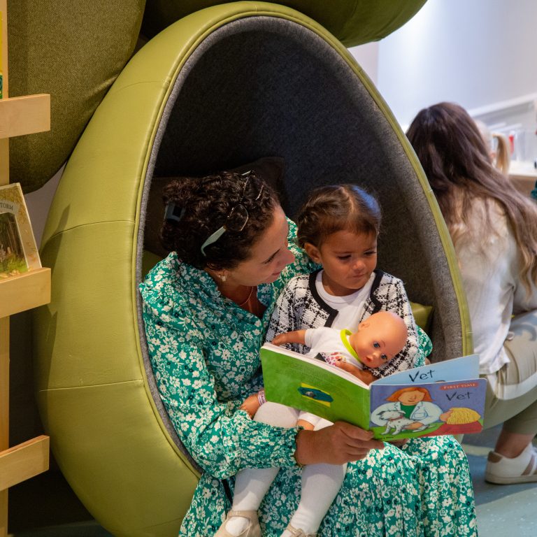 teacher and child sat on an egg-shaped seat, reading