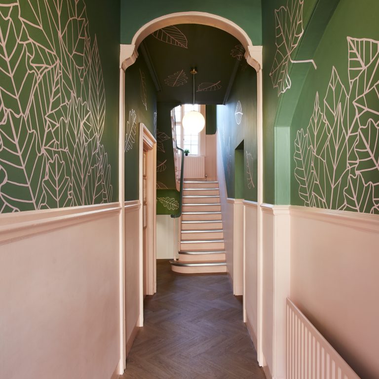 narrow hallway with green and peach walls and a stairs at the end