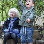 child pointing to the sky with another child sat on a stump