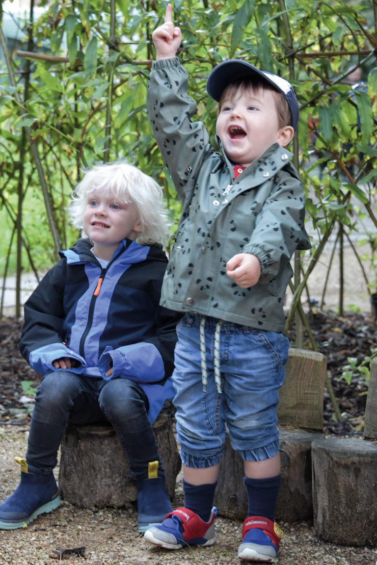 child pointing to the sky with another child sat on a stump