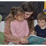 2 children reading a book with the teacher