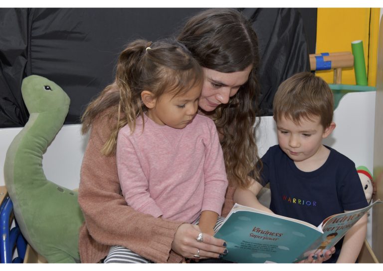 2 children reading a book with the teacher