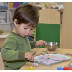 boy in khaki jumper using tools to work with clay