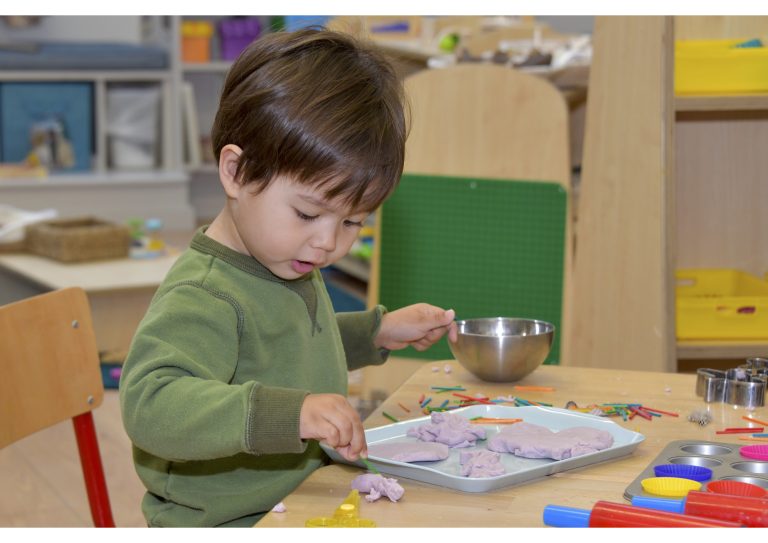 boy in khaki jumper using tools to work with clay