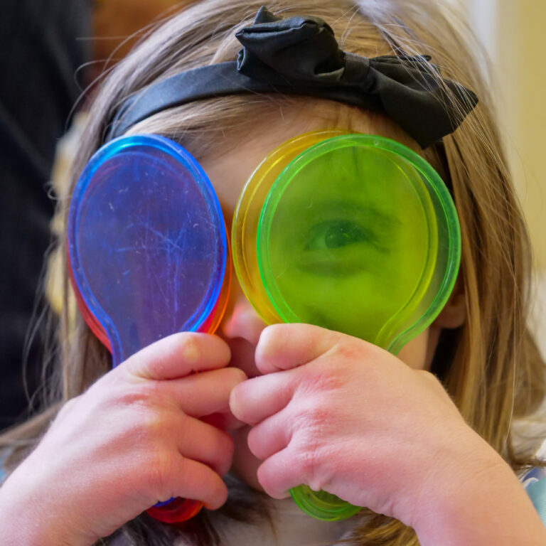 girl looking through coloured spoons